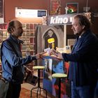 Zwei Männer tauschen eine "fakt" Karte aus. Im Hintergrund steht "Wenn Sie mich fragen" und "kino".