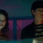 Zwei Personen schauen ernsthaft auf einen Bildschirm. Neonlicht beleuchtet ihre Gesichter in blau und pink.