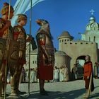 Ein Ritterschild zeigt einen Schwan. Soldaten in Rüstung stehen vor einer Festung mit Kuppeln im Hintergrund.