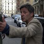 Ein Mann gestikuliert auf einer Straße, ein weiterer steht daneben mit einem Fahrrad, eine Frau schaut aufmerksam.