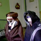 Zwei Figuren in mittelalterlichen Kostümen in einem grünen Raum mit Bett, Bilderrahmen und Holzkommode mit Dekoration.