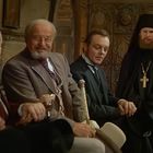 Sechs Männer in viktorianischer Kleidung und mönchischen Gewändern sitzen zusammen.