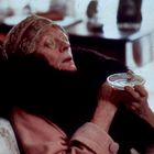 Ich kann das nicht erkennen. Eine ältere Person sitzt, mit Gurkenscheiben auf den Augen und einem Becher in der Hand.