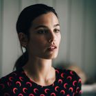 Kein Text. Eine Frau mit einem schwarzen Oberteil, das mit roten Halbmond-Motiven bedruckt ist. Hintergrund unscharf.