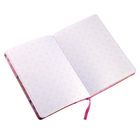 Ein aufgeschlagenes Notizbuch mit rosa geometrischem Dreiecksmuster auf weißen Seiten und einem rosa Leseband.