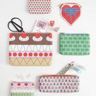 Verschiedene bunte Etuis mit Mustern, darunter Herzen, Schleifen und grafische Designs. Büroklammern und Scheren sind sichtbar.