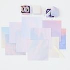 Es gibt keinen sichtbaren Text. Pastellfarbene Papierbögen, zwei offene Boxen mit Klebeband, eine geschlossene Box, ein Falzbein.