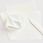 Es gibt keine sichtbaren Texte. Ein geometrischer Papieranhänger liegt auf mehreren Papierblättern, daneben ein Stift.