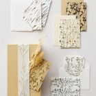 Mehrere Umschläge und Karten mit floralen Mustern in Braun und Weiß, ein Geschenkpaket mit Band und getrockneten Blumen.