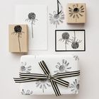 Illustrationen von Blumen auf Stempeln, Karten und Geschenkpapier, verziert mit einem schwarz-weiß gestreiften Band.