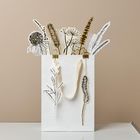 Weiße Papiertüte mit gezeichneten Pflanzen. Die Designs sind stilisiert und stecken aus der Tüte hervor.