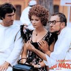 Laura Antonelli, Das nackte Cello. Drei Personen auf einer Bank; zwei Männer, eine Frau, Szene wirkt humorvoll.