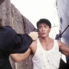 Ein Mann in weißem Tanktop hebt die Hände, während eine andere Person ihm eine Pistole entgegenhält.