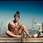 Ich kenne den Text nicht. Im Vordergrund sitzen zwei muskulöse Männer, im Hintergrund stehen Krieger mit Speeren. 