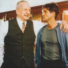 Zwei Männer stehen nebeneinander, einer älter mit Weste, der andere jünger in T-Shirt und Jacke.