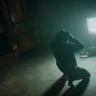 Keine erkennbaren Texte zu sehen. Eine Person kniet verzweifelt vor einem eingeschalteten alten Fernseher in einem dunklen Raum.