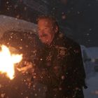 Ein Mann in einer Sheriff-Uniform feuert eine Waffe im Schneegestöber ab, während andere Personen im Hintergrund sichtbar sind.