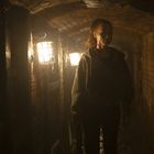 Eine Frau geht durch einen schmalen Ziegelgang mit schwachem Licht aus antiken Laternen.