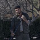 Ein Mann in Outdoor-Kleidung hält eine Schaufel. Er trägt Handschuhe, im Hintergrund sind karge Bäume.