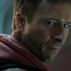 Es sind keine Texte sichtbar. Ein Mann schaut über die Schulter, trägt einen roten Hoodie und hat einen entschlossenen Blick.