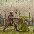 Vier Personen in märchenhaften Kostümen umgeben von blühenden Kirschbäumen. Ein Mann trägt einen Mondhut.