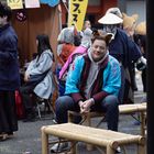 Schilder mit japanischen Schriftzeichen, bunte Kostüme, Menschen mit Tierohren und Gesichtsbemalung, fröhliche Atmosphäre.