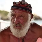 Kein Text vorhanden. Ein älterer Mann mit weißem Bart und bunter Mütze schaut nachdenklich in die Ferne.