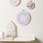 Florale Stickerei in Stickrahmen an der Wand, zart pastellfarbene Blumenmuster und Wanddekorationen.