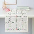 Stapel von Büchern mit "THE KINFOLK HOME" oben. Darunter ein Tischläufer mit Blumenmuster, daneben rosa Glas und Kerzenhalter.