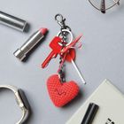 Roter Schlüssel mit "Yale," Herzanhänger. Lippenstift, Uhr, Brille, Notizblock, Lutscher und Stift auf grauem Hintergrund.