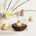Filzdeko: Küken, Hase, Blumen und Nester aus Filzwolle in einer Vase und auf einem Tisch arrangiert.