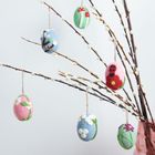 Es sind keine Texte vorhanden. Bunte Filz-Eier mit Blumendesigns hängen an Weidenzweigen in einer Vase.