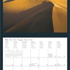 Kalenderseite für Mai in mehreren Sprachen. Oben: Foto von goldenen Sanddünen unter blauem Himmel. Unten rechts: Geo-Logo.