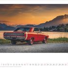 Die Zahlen 1 bis 31 sind am unteren Rand angeordnet. Ein roter Oldtimer steht vor einem See bei Sonnenuntergang. Bergkulisse im Hintergrund.