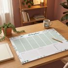„Wochenplaner“ mit Wochentagen und Notizzeilen. Auf einem Tisch mit Pflanze, Tasse und Regal im Hintergrund.