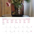 Kalenderblatt für November 2027 mit Blumengesteck in rotem Glas und verschiedenen Blüten vor Holzhintergrund.