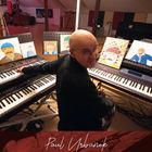 "Paul Urbanek." Ein Mann sitzt an zwei Keyboards. Vor ihm aufgestellte Gemälde zeigen bärtige Männer mit Hüten.