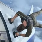 Ein Mann klammert sich mit Sauggriffen an die Außenwand eines in der Luft fliegenden Flugzeugs fest.