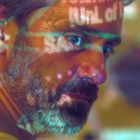 Ein Mann mit Bart betrachtet etwas intensiv. Sein Gesicht zeigt Lichter und unscharfe Buchstabenprojektionen.