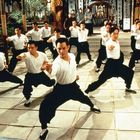 Männer in weißen Hemden und schwarzen Hosen üben Kampfkunst in einer traditionellen Halle.