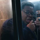 Ein Mann mit Brille spricht aufgeregt in einer Telefonzelle in den Hörer eines Münztelefons.