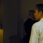 Ein Mann im Anzug sticht mit einem Messer im Rücken hervor. Gedämpftes Licht mit Lampen im Hintergrund.