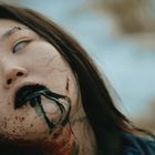 Ich kann keine Texte auf diesem Bild erkennen.  
Eine bleiche Person mit blutverschmiertem Gesicht und schwarzen Adern.