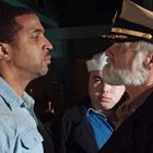 Zwei Männer stehen sich intensiv gegenüber. Der eine trägt eine Uniform mit Kapitänsmütze, umgeben von Matrosen.