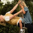 Ich kann den Text nicht lesen. Eine Frau mit Kind schaukelt lächelnd im Grünen.