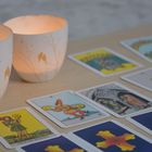 Mehrere Tarotkarten auf einem Tisch, begleitet von zwei leuchtenden Teelichtern in verzierten weißen Haltern.