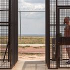 Zwei tätowierte Männer in weißen Shorts stehen sich in Metallkäfigen gegenüber, im Hintergrund ein Zaun.