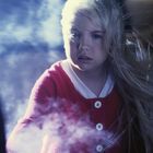 Ein Kind mit blondem Haar und rotem Pyjama schaut fokussiert, umgeben von einem nebligen, mystischen Dunst.