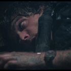 Es gibt keine ersichtlichen Texte. Eine Person liegt erschöpft am Boden, ihr Gesicht und Arm sind sichtbar.