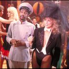 Zwei verkleidete Personen in einer festlichen Umgebung; einer in einer Uniform, der andere im Frack und Zylinderhut.